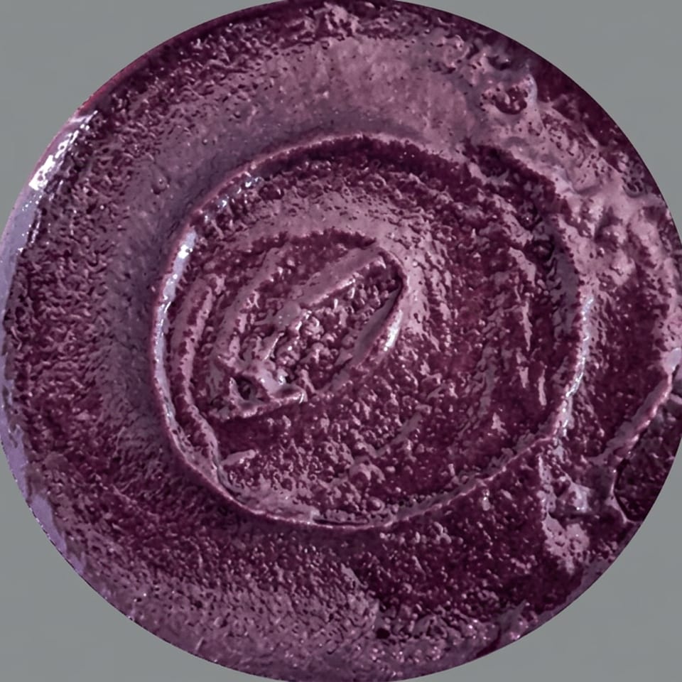 Purple-toned plated dish featuring concentric sauce patterns and a textured central garnish.
