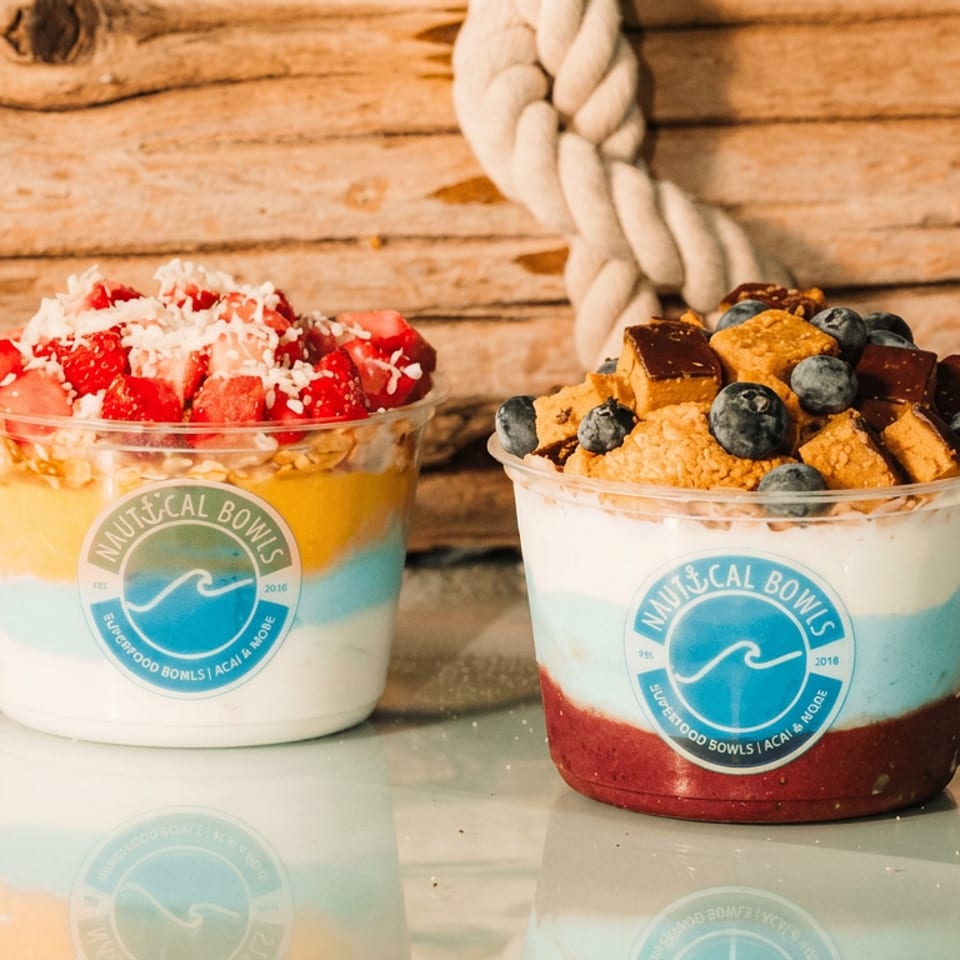 Two colorful acai bowls topped with strawberries, shredded coconut, blueberries, and granola on a rustic wooden table.
